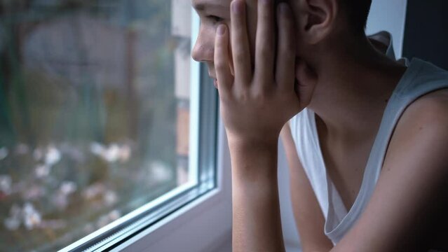 sad boy sitting inside and looking out the window, misses someone