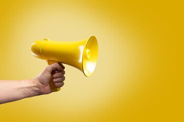 Yellow megaphone in a man's hand on a yellow background. Propaganda, rumors, election debates,...