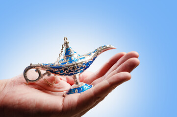 Aladdin's magical lamp in a woman's hand on a pale blue background. Close-up. Minimalism. Oriental fairy tales, wealth, luck, treasures. Advertising, banner.