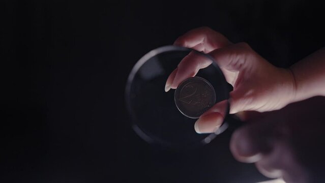 examination of a 2 euro coin under a magnifying glass on a black background close-up