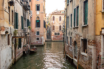 Fototapeta na wymiar Narrow canal with medieval buildings, stone walkway and bridge reflected in calm water in Venice, Italy on sunny day.