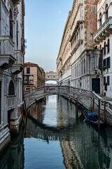 Narrow canal with medieval buildings, and Bridge of Sighs reflected in calm water  in Venice, Italy on sunny day.