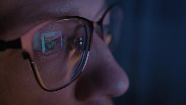 man with glasses works at a computer in the evening at home, glare on glasses, receives multimedia information