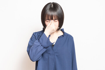 目が疲れて目頭をつまんでいる若い女性