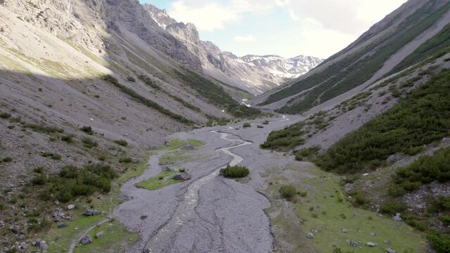 Aerial drone footage slowly twisting and descending in a dramatic glacial valley surrounded by a steep mountains and pine trees with patches of snow and an alpine river in Switzerland.