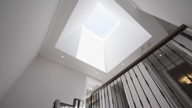 Pan and tilt shot from staircase to the flat roof window on the ceiling in a house during a sunny day