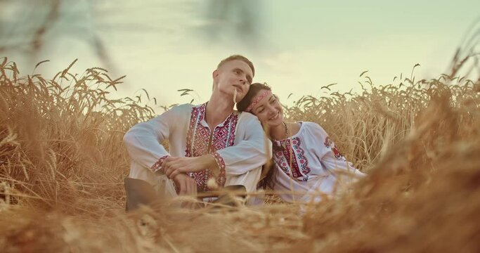 Man and a woman Slavs are sitting in a field, a woman put her head on a man's shoulder. Loving couple of Slaves are resting in the field and dreaming. Beautiful landscape with golden ears. 4k, ProRes
