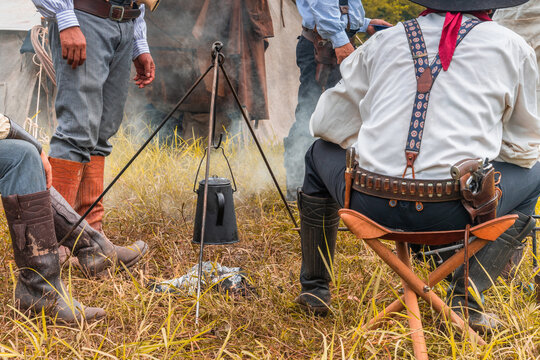 Cowboys  have outdoor camping.
kettle is heated on a bonfire.Outdoors camp fire with kettle.Outdoors camp fire .avenger style.