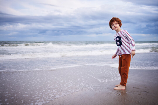 cute redhead boy having fun at the beach, walking along the ocean shore