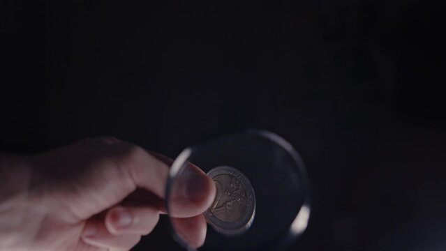 examination of a 2 euro coin under a magnifying glass on a black background, coin authenticity check, close-up