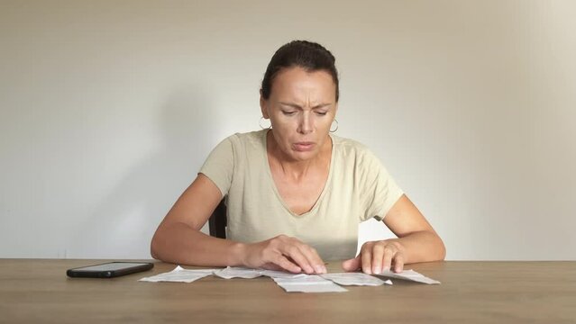 Female crisis bills for home appliances. An upset woman count electrical and gas bills on the table. A concept of expensive energy costs and inflation in Europe.