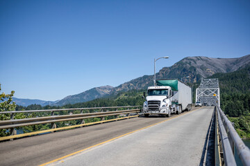 Local day cab big rig semi truck transporting cargo in bulk semi trailer driving on the truss...