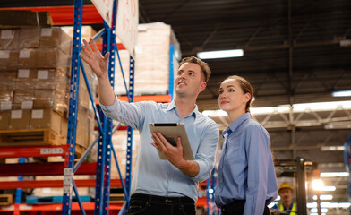 Obraz premium Warehouse manager talking and pointing towards shelf while checking product in warehouse, Logistic industry concept.