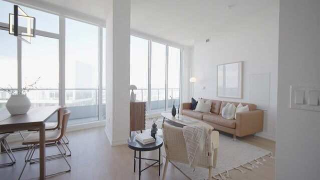 Wide angle push in shot No.1 showing the dinning and living area of a high ceiling penthouse condominium unit with a floor to ceiling window wall at the back and balcony outside during a sunny day
