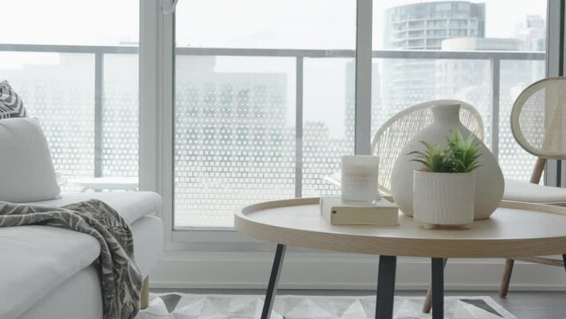 Detail shot of a decorated coffee table and couch beside the floor to ceiling windows in the living area of a condominium with the balcony at the background unit during a sunny afternoon.