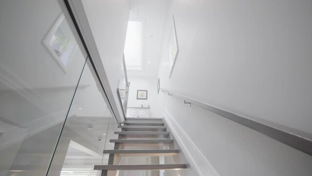 Going upstairs through a see through glass stair wall in a tilt cemara angle to show the flat roof window at the second floor ceiling in a house