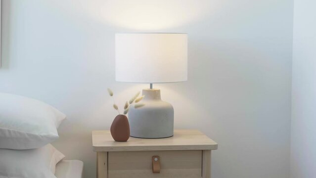 Dolly shot of the nightstand and lamp beside the bed in a condominium bedroom during a sunny day