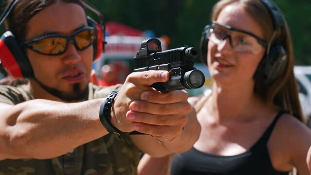 Dynamic closeup portrait of a handsome caucasian man in moro t-shirt and protective gear holding a black gun and shooting at the target. Beautiful sunny weather. Gun range concept. High quality 4k