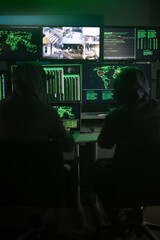 Two hooded hackers hacking security firewall late at night in basement hideout. Vertical image.