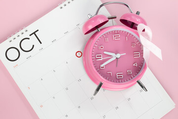 Fototapeta na wymiar Pink bow ribbon is attached on pink alarm clock and put on calendar to encourage breast cancer campaign