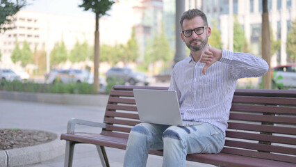 Thumbs Down by Young Adult Man with Laptop Sitting on Bench