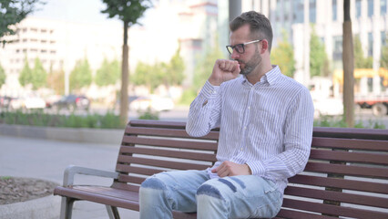 Young Adult Man Coughing while Sitting on Bench Outdoor
