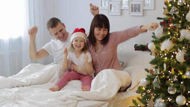 family, love and christmas concept - young parents having fun with little daughter in bedroom near  decorated christmas tree