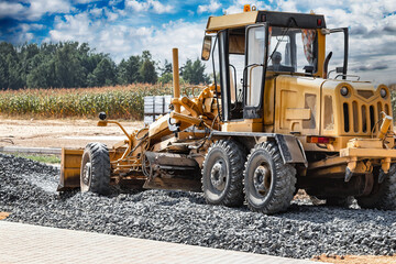 Road grader at the construction site. Powerful construction machine for ground leveling and excavation. Close-up. Professional construction equipment. - obrazy, fototapety, plakaty