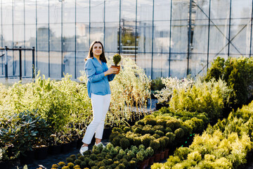 A young woman stands outside a plant shop and chooses a pot with a small tree. A woman chooses plants for landscaping the yard. Home gardening concept