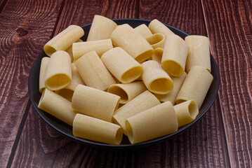 Traditional Italian uncooked Paccheri Pasta from Gragnano on wooden table.