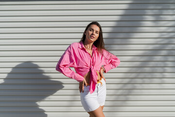 Young beautiful brunette woman in a pink shirt and white denim shorts against the background of a...