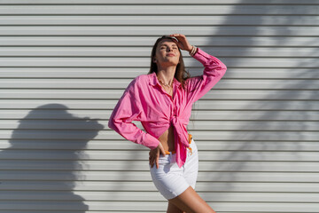 Young beautiful brunette woman in a pink shirt and white denim shorts against the background of a...