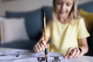 Cute little caucasian girl seven years old with blonde hair writing Chinese characters at home