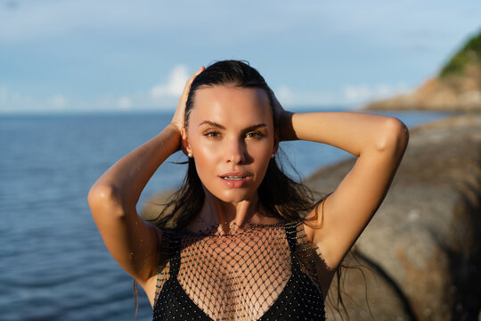 Young beautiful tanned woman on the background of the sea at sunset in a black swimsuit and a mesh dress
