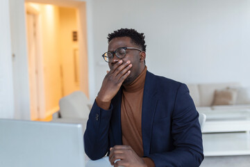 Tired man yawning after long working day . Early morning working. Sleepy tired freelancer is yawning at his home in front of the laptop`s screen on desk top