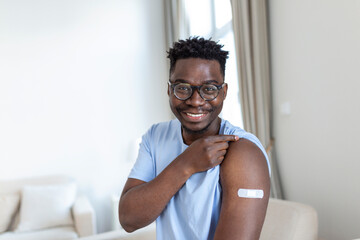 Portrait of a man smiling after getting a vaccine. African man holding down his shirt sleeve and...