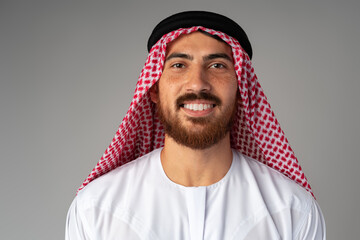 Portrait of smiling young Arab man on gray background