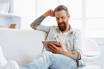 Handsome bearded man using digital tablet while resting on couch at home
