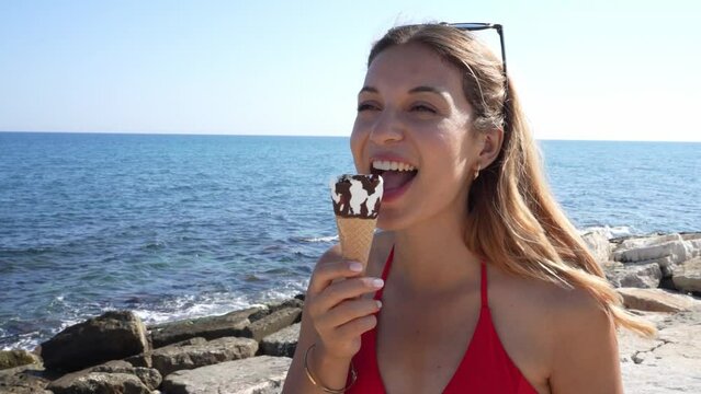Close-up of attractive bikini woman eating an ice cream cone italian gelato turns around to the camera on the beach on summer