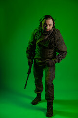 soldier in the studio on a green background with colored light. a man in military uniform with a gun, rifle or machine gun. military. airball player