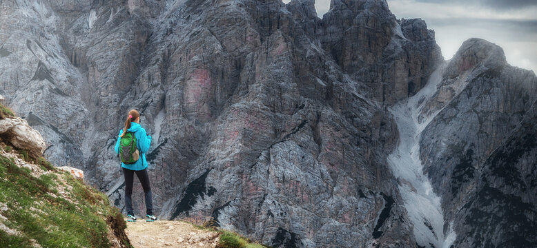Travel and tourism concept. Young woman with backpack standing over a cliff and looking at the beautiful mountains. Beautiful landscape with sporty female standing her back
