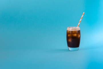 Iced black coffee in a tall glass with a paper orange straw on the isolated blue background