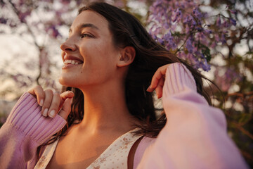 Tender young caucasian girl smiling looking away spending time outdoors among flowering trees. Brunette loses her hair, wears spring clothes. Vacation concept.