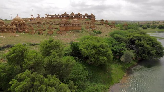 Drone Flying Over Lakeside Trees Towards Hillside Bada Bagh Temple In Jaisalmer Beside Lake. Dolly Forward
