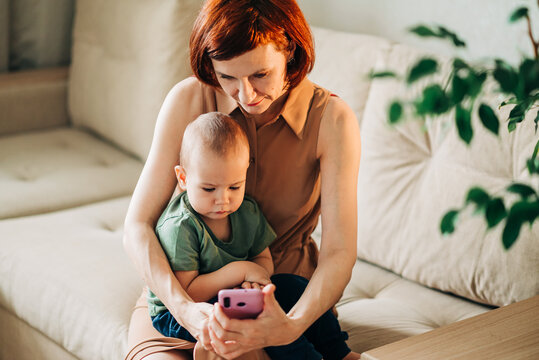 Mom with baby watching to smart mobile phone videos or work text