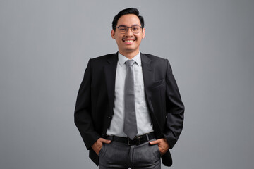 Portrait of smiling handsome young businessman in formal suit feeling relaxed and confident, looking at camera isolated on grey background