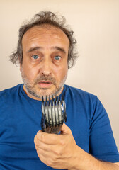 desperate looking man with partially cut hair looks at hair trimmer failed during use