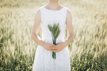 Carefree woman enjoys nature in a wheat field and touches ears of ripe yellow wheat with her hand....