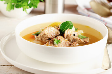 Autumn winter warming beef broth with a piece of meat and vegetables in a white dish on light background.