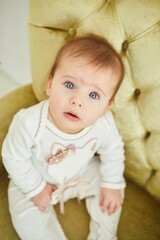 Fototapeta premium A little baby girl in white clothes is sitting on a chair. The concept of motherhood and childhood.